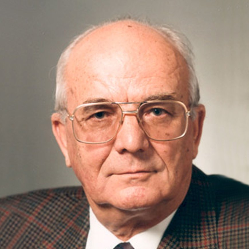 Das Porträt im Nahaufnahme zeigt Karl Späh mit randloser Metallbrille und einem karierten Anzug, der ernsthaft in die Kamera blickt