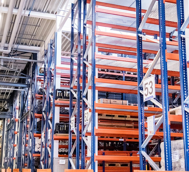 Das Bild zeigt eine lange Reihe hoher, blauer und orangeroter Hochregale in einer Lagerhalle von Späh, die mit Materialien und gekennzeichneten Waren (z.B. mit Regalnummern 51, 52 und 53) gefüllt sind.