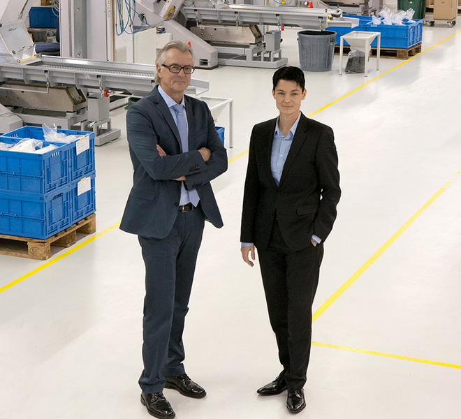 Das Porträt zeigt links Alfred Späh in einem hellblauen Hemd und einem grauen Anzug und rechts Sandra Späh in einem dunklen Anzug, wie sie in einer hellen Produktionshalle der Firma stehen.