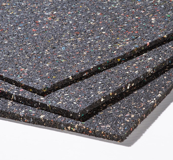 Drei gestapelte Platten aus schwarzem Gummigranulat mit farbigen Sprenkeln sind in einer Detailansicht der Materialoberfläche zu sehen.