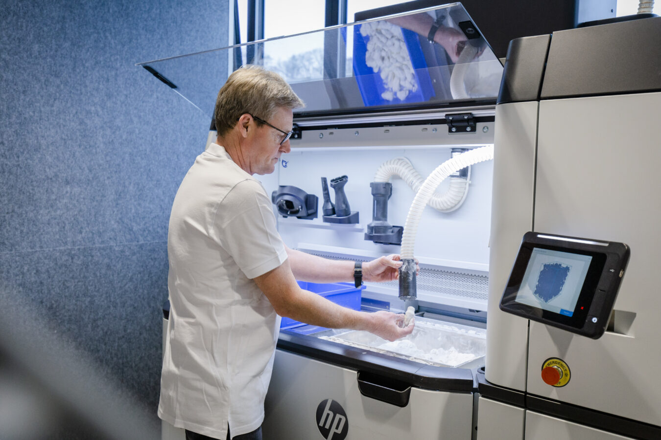 Ein Mitarbeiter im weißen Shirt saugt weißes Pulver von einem Teil in einer HP-Fertigungsstation für die additive Produktion.