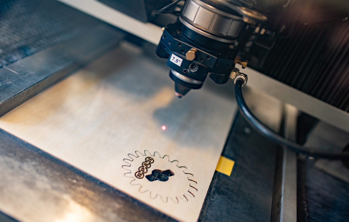 Ein Laserschneidkopf graviert ein zahnradförmiges Späh-Logo präzise in eine helle Platte.