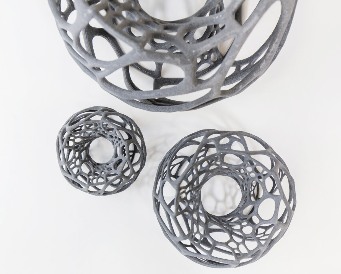 Drei graue, filigrane, gitterartige Kugeln, die im 3D-Druckverfahren von Späh gefertigt wurden, liegen auf einem weißen Hintergrund.