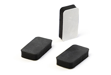 Zu sehen sind drei kleine, rechteckige Schaumstoffpuffer, von denen einer die weiße Klebefläche auf der Unterseite präsentiert.
