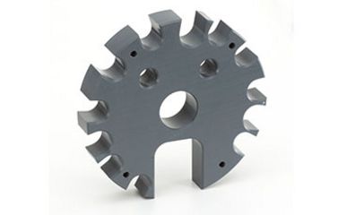 Ein massives, zahnradähnliches Bauteil aus grauem Kunststoff mit verschiedenen Bohrungen und Aussparungen liegt als gefertigtes Präzisionsteil auf einem weißen Hintergrund.