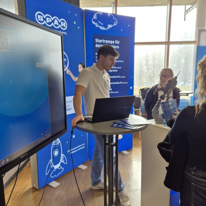 Ausbildungsmessestand der Karrierebörse an der FH Albstadt-Sigmaringen. Es wird an einem großen Bildschirm ein Kommunikationsspiel gespielt