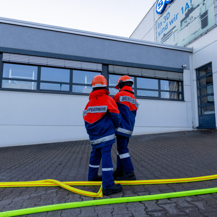 Zwei Jungen aus der Jugendfeuerwehr stehen vor dem Späh Gebäude und halten gemeinsam einen Schlauch.