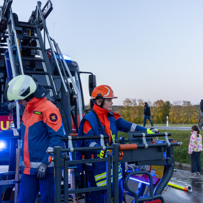 Zwei Mitarbeiter der Jugendfeuerwehr stehen im Korb der Drehleiter. Der eine Mitarbeiter öffnet den Korb und verlässt ihn.