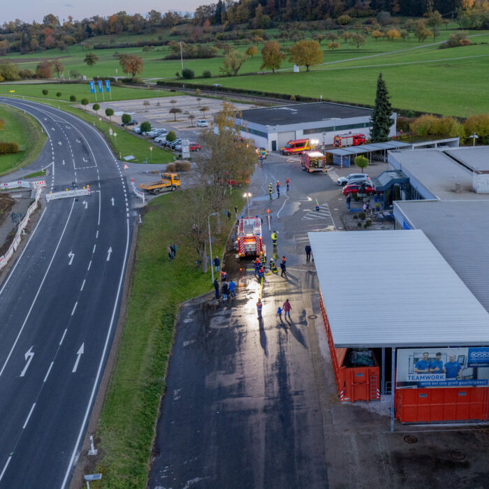 Auf dem Späh Gelände stehen mehrere Kinder aus der Jugendfeuerwehr und Erwachsene aus der Feuerwehr für eine Übung. Dort sind mehrere Feuerwehrfahrzeuge auf dem Gelände verteilt.