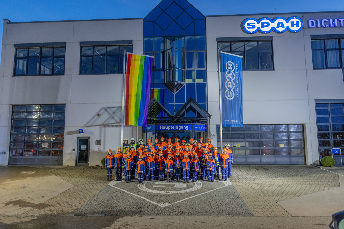 Gruppenfoto von vielen Kindern aus der Jugendfeuerwehr vor dem Haupteingang von Späh. Alle Kinder sind einheitlich in ihrer Jugendfeuerwehrkleidung.