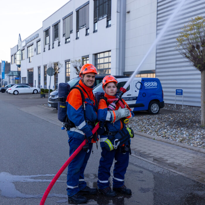 Zwei Jungen aus der Jugendfeuerwehr stehen vor dem Späh Gebäude und geben mit dem Schlauch ein Strahl in die Luft ab.