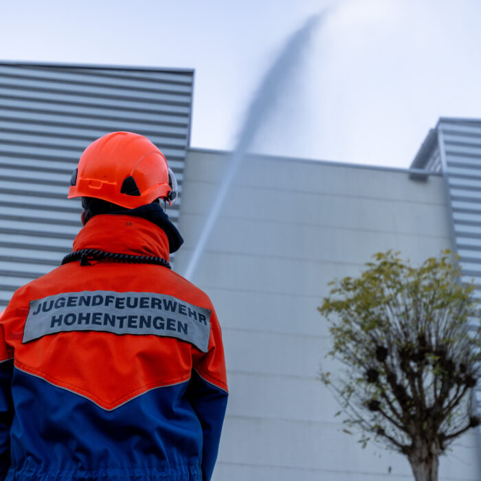 Ein Kind aus der Jugendfeuerwehr steht vor dem Späh Gebäude und schaut zu wie ein Strahl abgegeben wird auf das Gebäude.