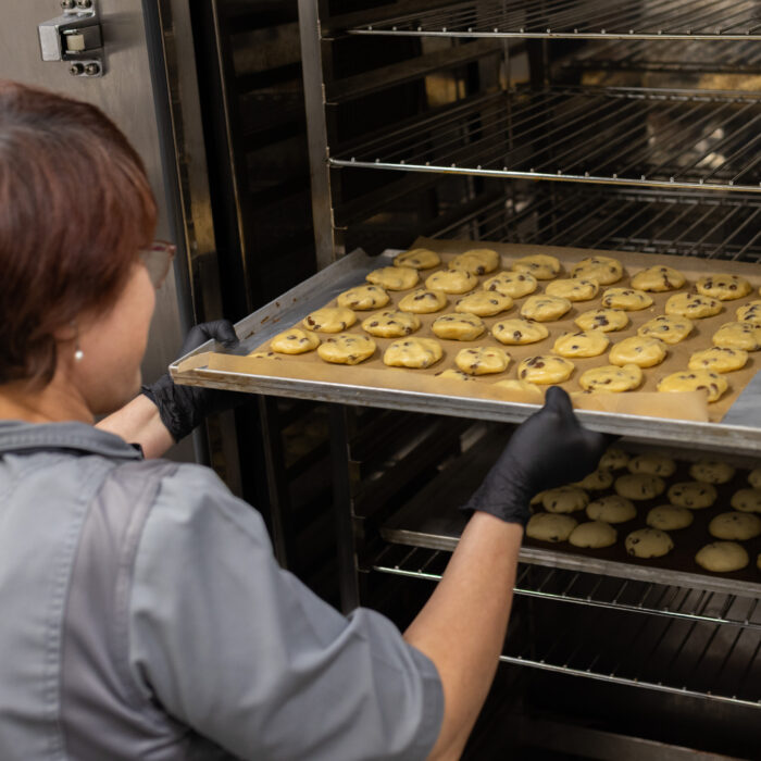 Eine Späh-Mitarbeiterin aus der Kantine schiebt ein Backblech mit Weihnachtsgebäck in den Ofen.