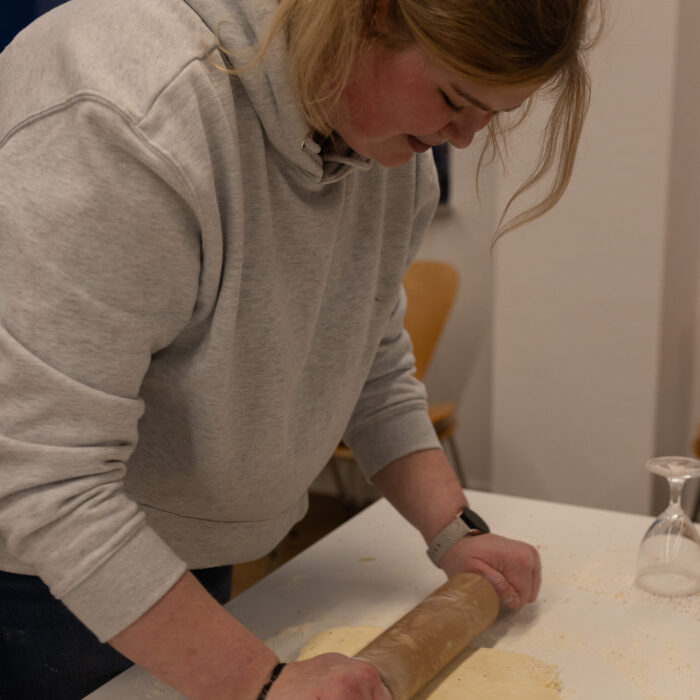 Eine Späh-Mitarbeiterin ist an einem Tisch und rollt den Teig aus mit einem Teigroller.