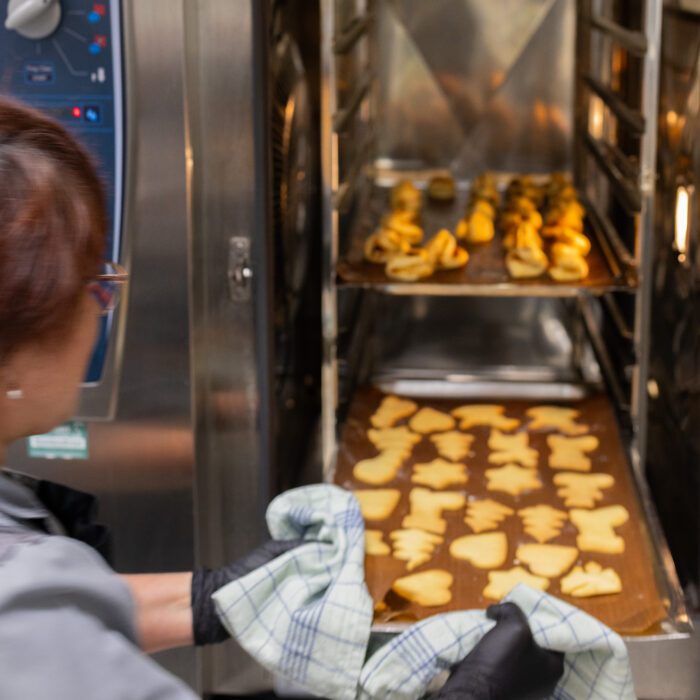 Eine Späh-Mitarbeiterin aus der Kantine schiebt das untere Backblech voller Weihnachtsgebäck aus dem Ofen. Das obere Blech liegt noch im Ofen.