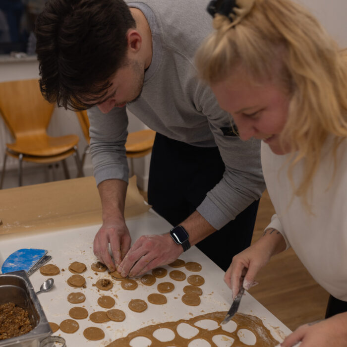 Zwei Späh-Mitarbeiter backen Weihnachtsgebäck zusammen. Ein Mitarbeiter sticht eine Form heraus und der andere Mitarbeiter verziert das Gebäck.