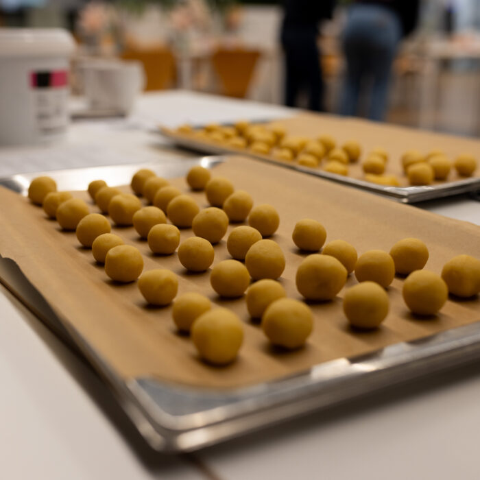Kugelförmiges Weihnachtsgebäck ist auf zwei Backblechen in der Kantine. Im Hintergrund sind mehrere Becher und zwei Späh-Mitarbeiter die zusammen Backen.