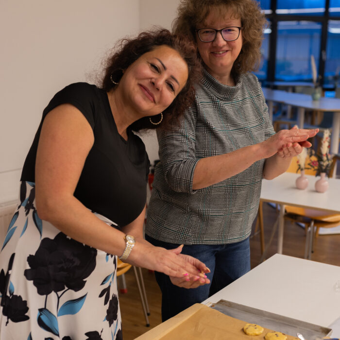 Zwei lächelnde Späh-Mitarbeiter backen zusammen Weihnachtsgebäck. Beide halten etwas Teig in ihren beiden Händen. Auf dem Backblech sind in form gebrachte Plätzchen.
